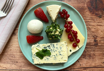 Different types of cheese with butter in parsley, strawberries and currants.