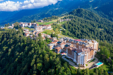 Fototapeta na wymiar Summer aerial view of the Ski Resort Rosa Khutor. A complex of hotels on the site of the former Olympic village of Rosa Plateau at an altitude of 1170 m from sea level. Krasnaya Polyana, Sochi, Russia
