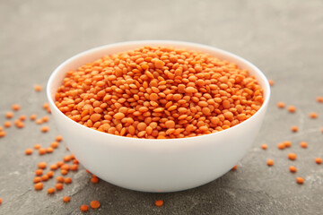 Red lentils in bowl on a grey wooden table.