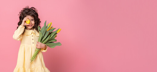 Funny child girl holding tulips and colorful Easter egg in front of her eye on pink background. Banner copyspace.
