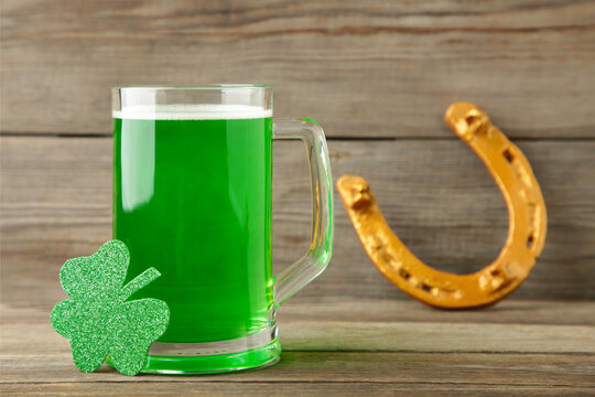 Glass of beer and horseshoe for St Patricks day on grey wooden background.