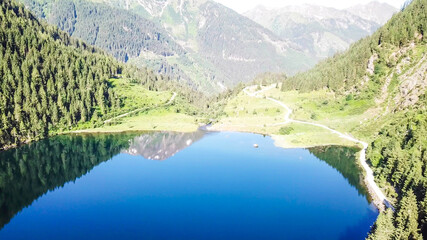 Fototapeta na wymiar Alpine lake seen from above. The lake is surrounded with Alps overgrown with forest. The surface of the lake is calm, it reflects the mountains and sky. Clear and sunny day. Schladming region, Austria