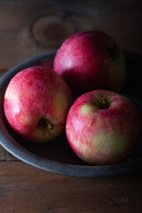 Fresh red apples in plate on wooden table.