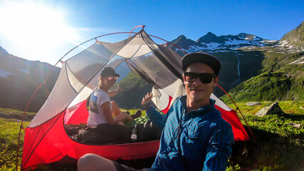 A couple camping in a wilderness. They sit in a small tent, placed on a top of a mountain peak,...