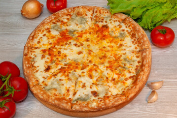 Four cheese pizza on a board with tomatoes and green salad
