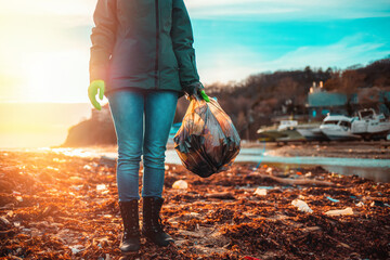 Day of Earth. A female volunteer stands on a muddy beach with a bag of garbage. Sunset