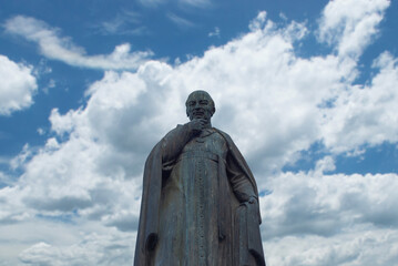 Estatua antigua de sacerdote en el centro de Querétaro, México con un cielo azul con nubes en el...