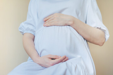 Pregnant woman in white dress holding belly with her hands.