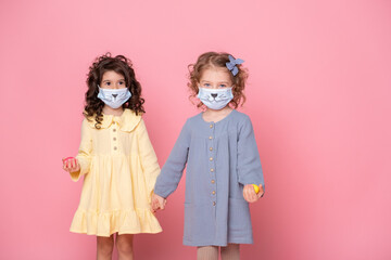 two girls in protective mask with colored eggs holding hands on pink background. Covid easter concept