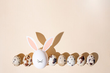Row of quail eggs with one egg in the form of an easter bunny on a beige background in the sunlight