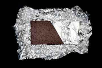 Sweet and delicious and yummy chocolate bar on silver foil on black background photo taken from above