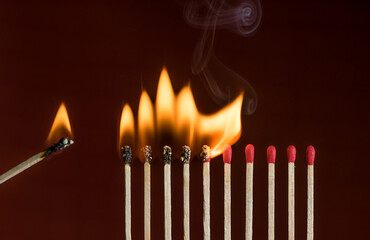 Lit match next to a row of lighting matches. Red phosphorus matches on dark red background. Concept...