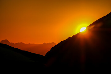 Sun setting behind a massive mountain range of Schladming Alps, Austria. The slopes are steep, partially covered with snow. Dangerous mountain climbing.Clear and beautiful view. Endless mountain range