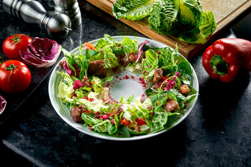 Warm salad mix with chicken liver and pomegranate served in a white plate on a dark marble background. Restaurant food.