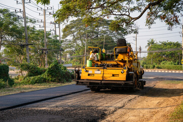 Yellow steamroller or soil compactor working on asphalt road at construction site
