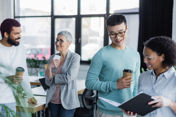 Multiethnic business people with coffee to go looking at paper folder