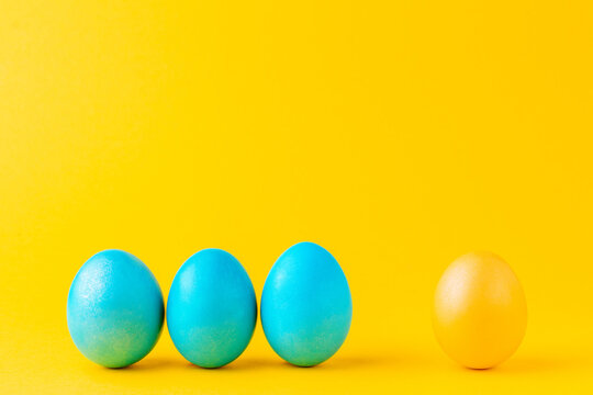 Three blue eggs against single yellow egg. Colorful Easter eggs in a row on yellow background. Difference concept.