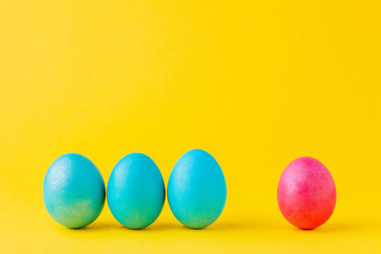 Leadership concept. Three blue eggs against red egg on yellow background.
