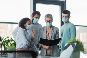 Multicultural businesspeople in medical masks and team lead working with paper folder