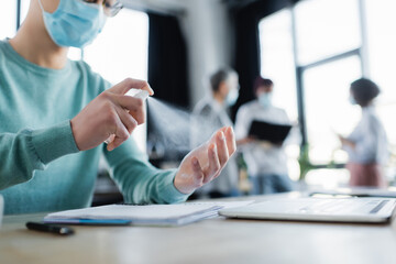 Cropped view of businessman in medical mask using antiseptic at table