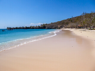 An areal, drone shot with a view on an idyllic Pink Beach on Lombok, Indonesia. Many boats drifting on a calm surface of the sea. Unspoiled, hidden gem. Perfect place for peaceful, relaxed holidays