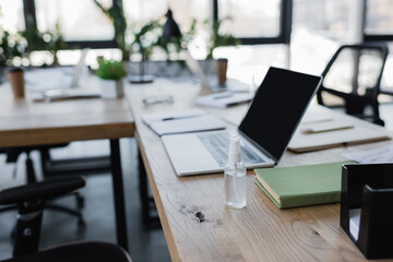 Sanitizer near book and laptop on office table