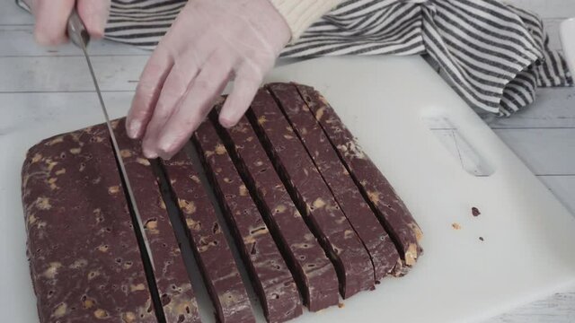 Step by step. Cutting homemade macadamia fudge on a white cutting board.