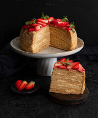 Homemade honey layer cake with fresh berries on a black background. Side view