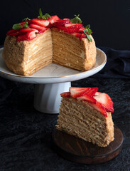 Homemade honey layer cake with fresh berries on a black background. Side view