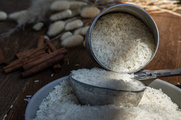 Thai jasmine rice pouring from old steel can with steel dipper on bowl on an old rustic wooden...