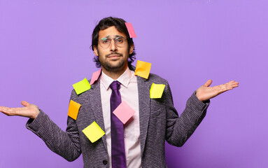 young handsome indian man feeling puzzled and confused, doubting, weighting or choosing different...