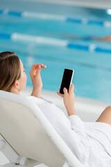 young woman resting on deck chair and holding smartphone with blank screen