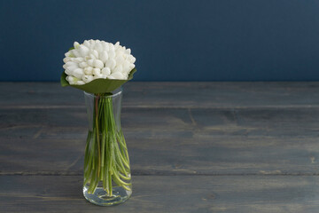 Little bouquet from white snowdrops in transparent vase on dark wooden and blue background, copy space for text. Greetings concept. Celebration of spring holidays.