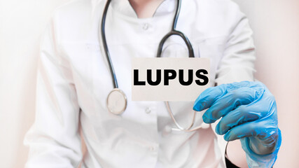 The doctor's blue - gloved hands show the word LUPUS - . a gloved hand on a white background. Medical concept. the medicine