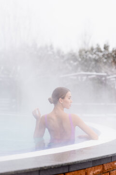 steam near young woman looking away and taking bath in outdoor hot spring pool