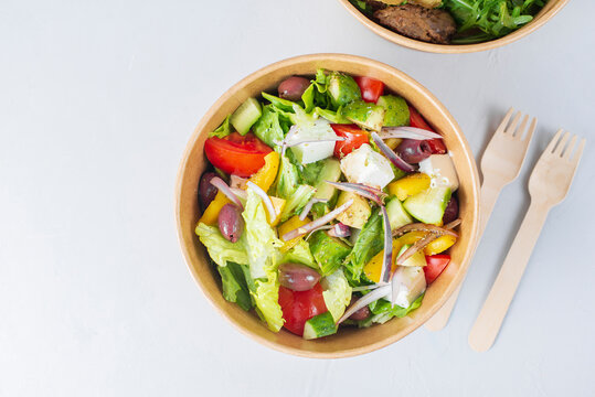 Diet Greek salad with feta, tomatoes, greens on light background top view. Healthy lunch. Food delivery in disposable plate of craft paper. Eco-friendly carton packaging environment protection