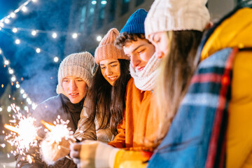 Happy girls and boy set fire to sparklers at night and laugh. Young people with beautiful lights. Girlfriends and boyfriend are travel. Rest during the holidays. Celebrating your life with fun.