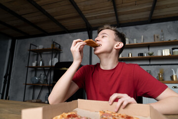 young man eating pizza sitting at a wooden table