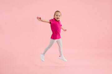 Fototapeta na wymiar Jumping, flying. Childhood and dream about big and famous future. Pretty little girl isolated on coral pink studio background. Dreams, imagination, education, facial expression, emotions concept.