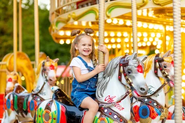 Fotobehang Amusementspark gelukkig babymeisje rijdt in de zomer op een carrousel op een paard in een pretpark