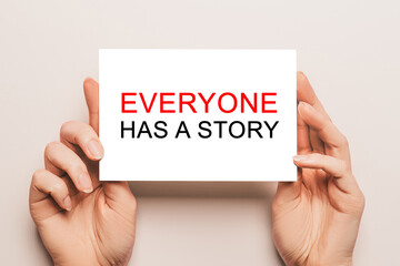 Female hands hold card paper with text Everyone has a story on a yellow background. Business and finance concept