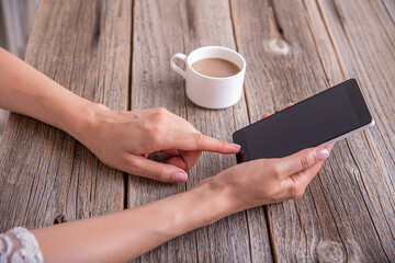 Smartphone in female hands on the background of a wooden table and a cup of coffee.
