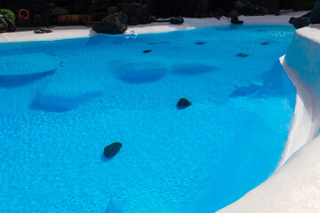 Intense blue swimming pool with volcanic rocks on bottom at Lanzarote landmark. Tourist attraction, nature integration in architecture concepts
