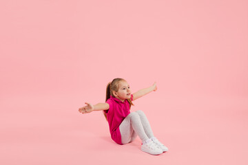 Showing, greeting. Childhood and dream about big and famous future. Pretty little girl isolated on coral pink studio background. Dreams, imagination, education, facial expression, emotions concept.