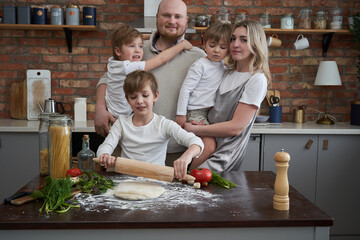 Two parents enjoy cooking with their children in the kitchen. Happy family and their domestic life and leisure activity.