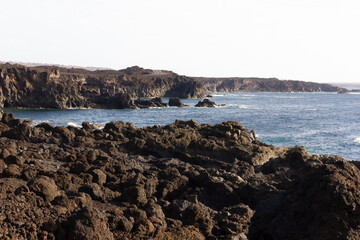 Volcanic coast on sunny day in Lanzarote. Black rocks cliffs by the sea. Summer vacation, travel destination, tourism concepts