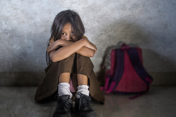 young scared and helpless 7 or 8 years old female child in school uniform suffering discrimination and harassment at school sitting on floor crying in bullying problem concept