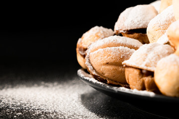 Biscuits with condensed milk in a dark plate, closeup on a black background, sprinkled with powdered sugar. Macro
