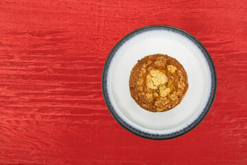 Overhead view of a single cinnamon crumb muffin on a plate atop a bright red wood painted background.