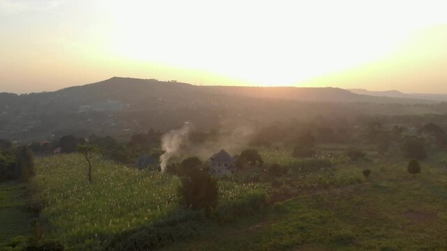 Aerial shot of lush beautiful landscape in rural Uganda with a mountain on the horizon and the sun setting.